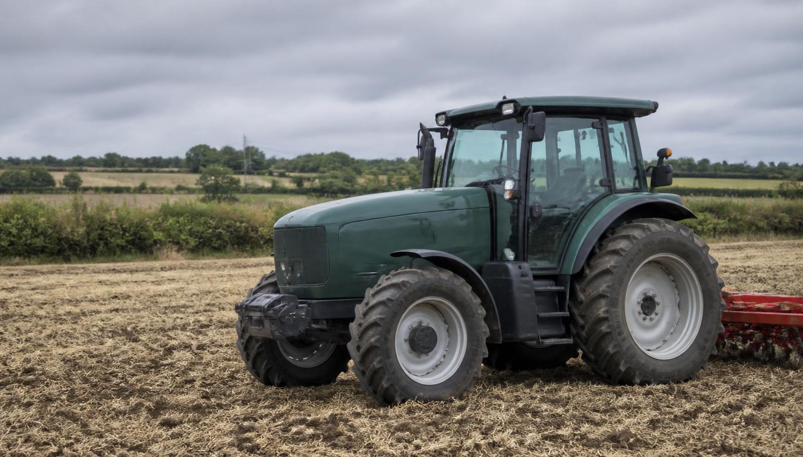 Compact tractor on a British field with hedgerows under an overcast sky